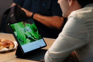Persona observa una pantalla con el mensaje “Cultivamos el futuro” en un sitio web de agricultura sostenible, junto a medialunas sobre la mesa.