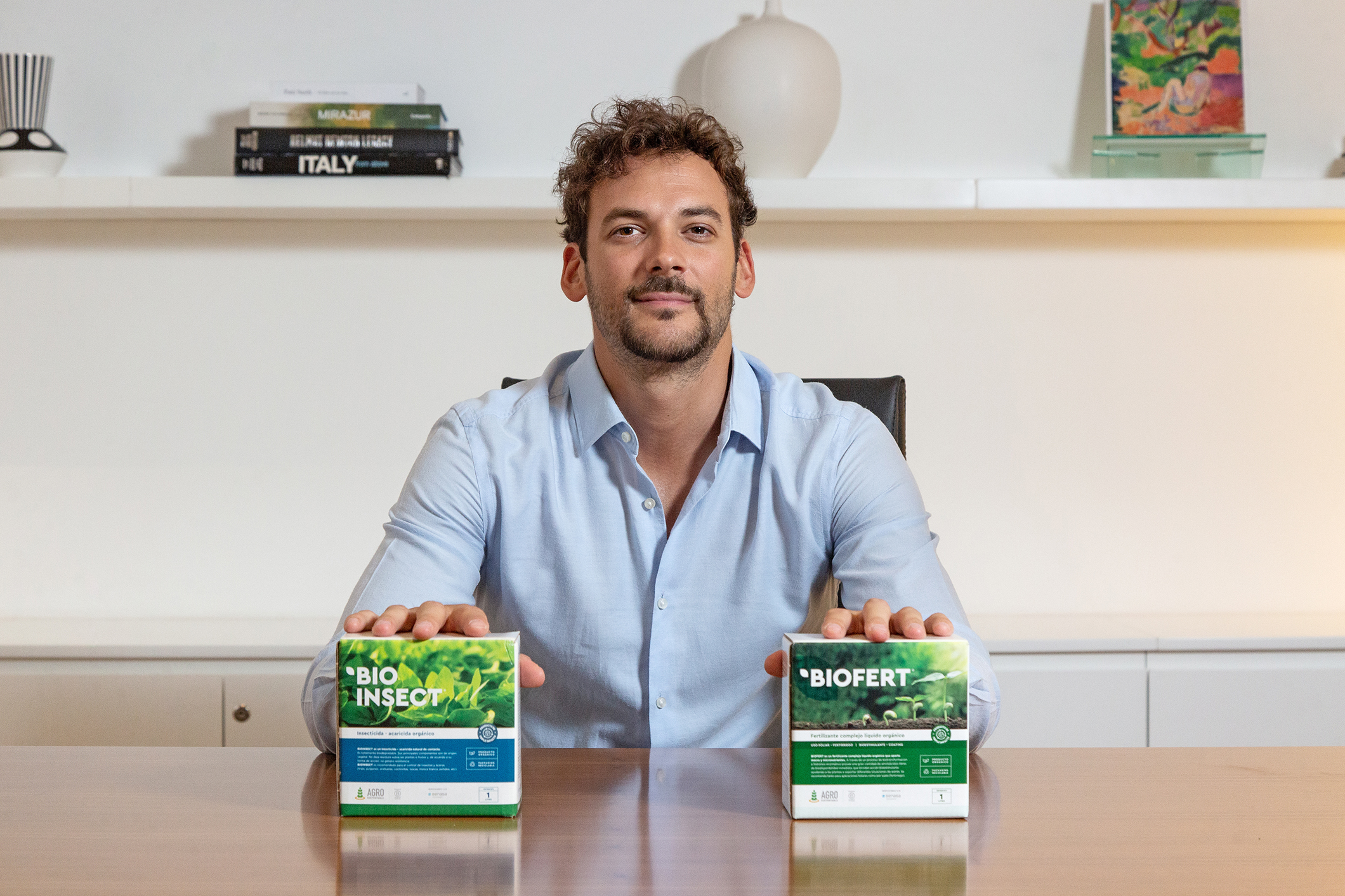Hombre sentado con cajas de bioinsumos BIOFERT y BIOINSECT sobre una mesa.