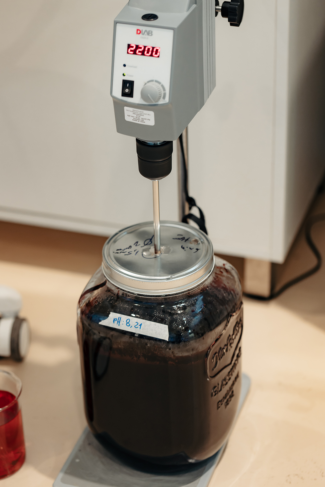 Frasco con bioinsumo líquido en proceso de agitación mecánica, con etiqueta de pH y equipo de laboratorio.