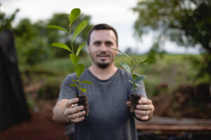 Hombre sosteniendo dos plantines con raíces expuestas en un entorno rural.